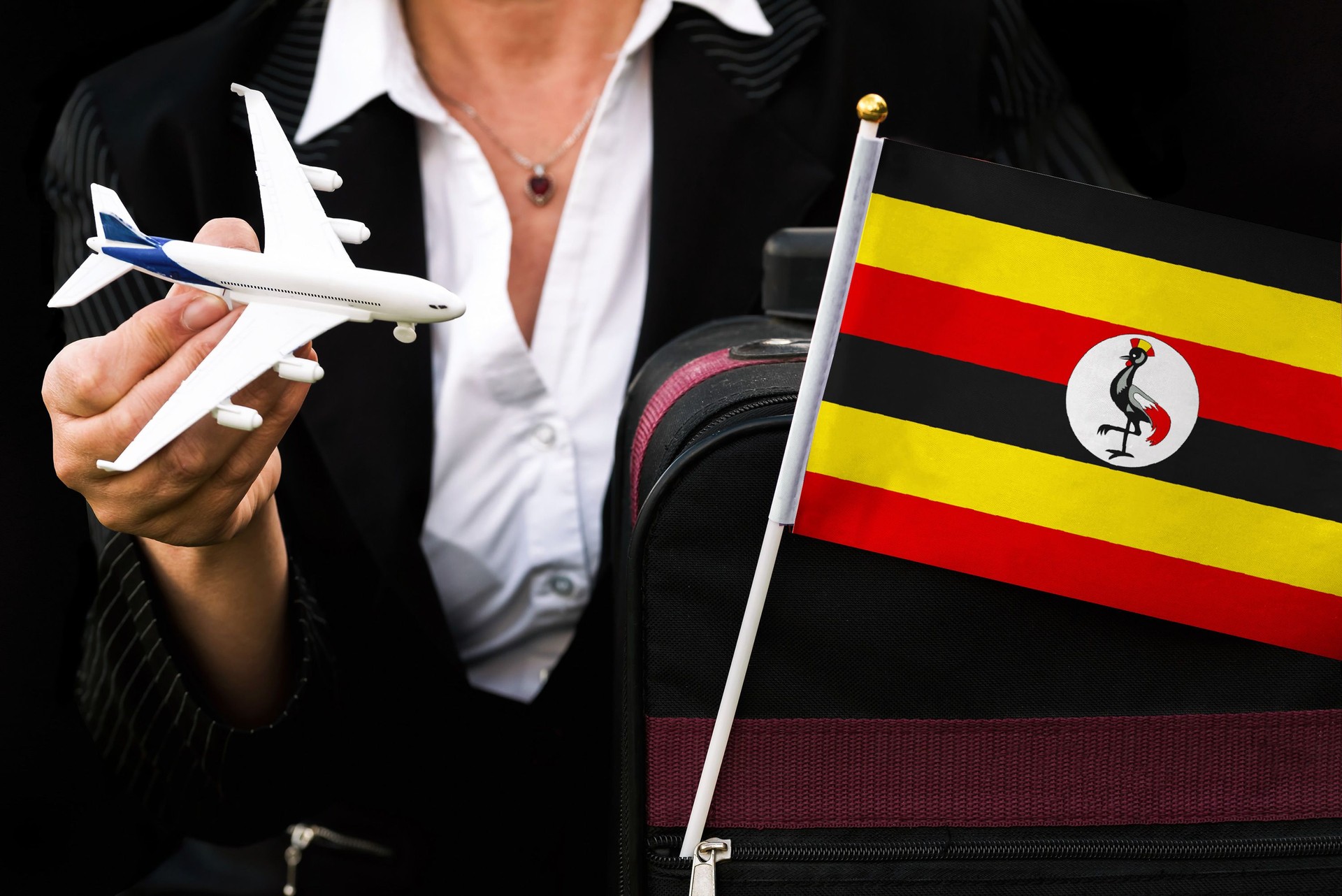 business woman holds toy plane travel bag and flag of Uganda