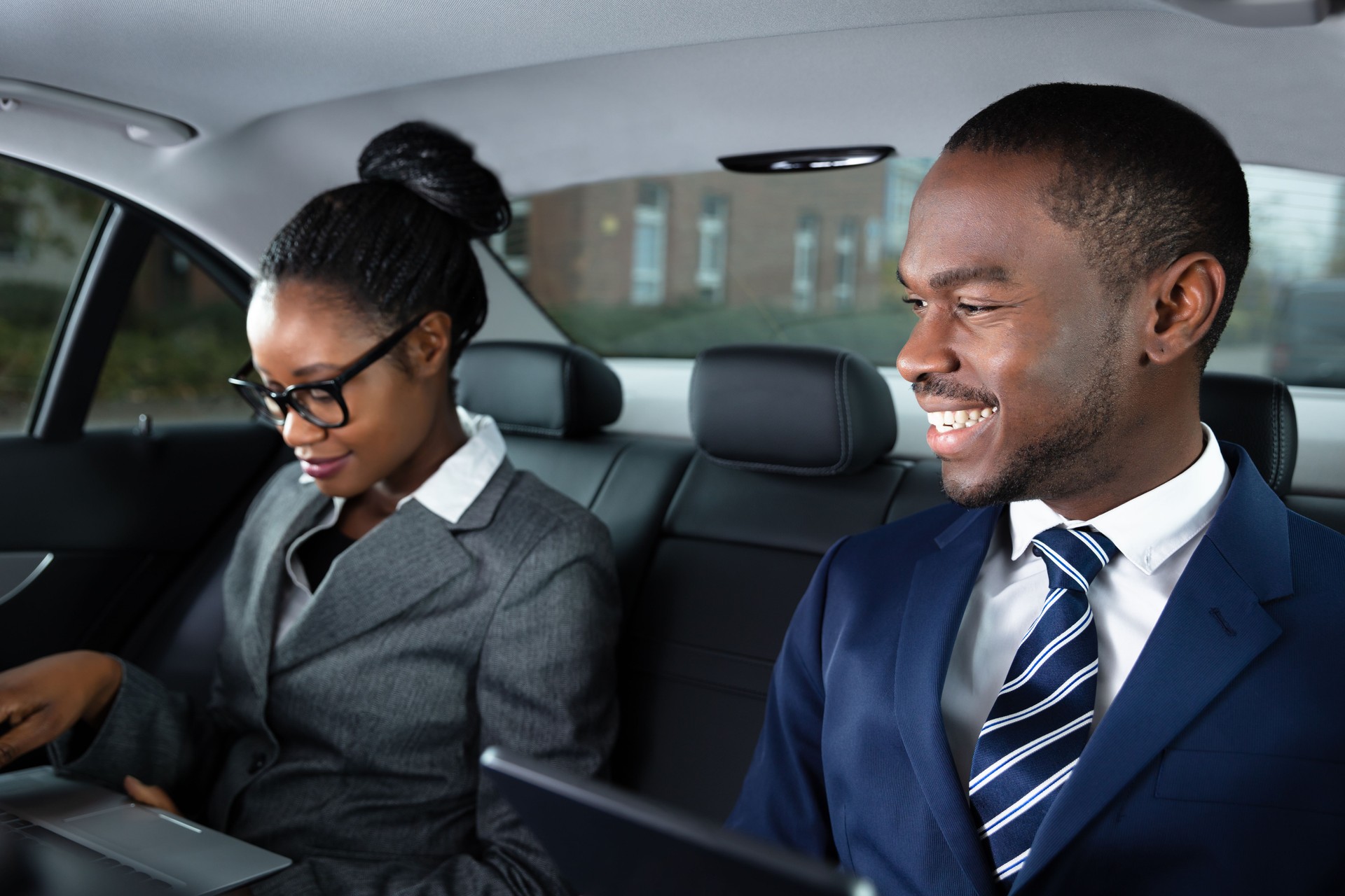 Two Businesspeople Sitting Inside Car Using Electronic Devices